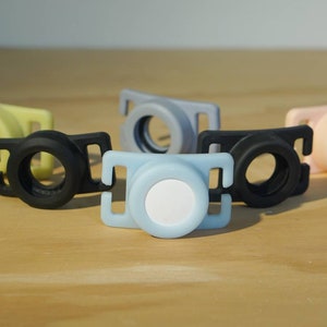 May include: Five different colored plastic camera lens caps. The caps are in various colors, including black, light blue, yellow, pink, and gray. The caps are designed to fit over the lens of a camera to protect it from dust and scratches.