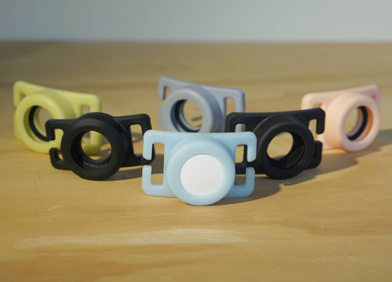 May include: Five different colored plastic camera lens caps. The caps are in various colors, including black, light blue, yellow, pink, and gray. The caps are designed to fit over the lens of a camera to protect it from dust and scratches.