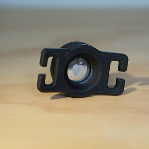 May include: Black plastic adapter with a circular opening featuring the Apple logo. The adapter has two loops on either side.