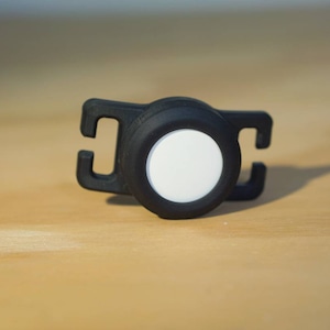 May include: A black and white safety light with a reflective surface. The light is attached to a black strap with a clip.