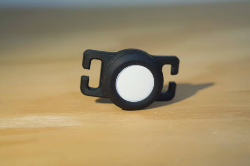 May include: A black and white safety light with a reflective surface. The light is attached to a black strap with a clip.
