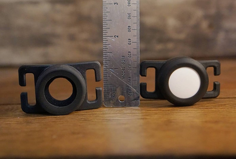 May include: Two black plastic clips with a white reflective disc on one and a black ring on the other. The clips are about 1 inch wide and are next to a ruler.