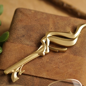 May include: An ornate gold-coloured key with a decorative, flowing design. The key is lying on a brown leather surface.