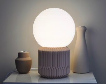 May include: A white globe lamp with a ribbed, light pink base. The lamp is on a white surface with two smaller, brown ceramic vases.