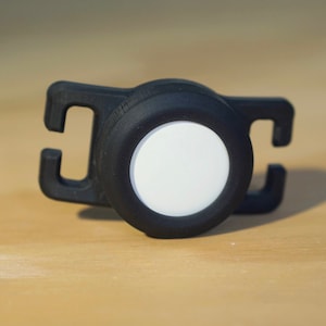 May include: A black plastic safety light with a white reflective disc. The light has a clip for attaching to clothing or a backpack.