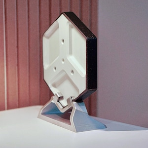 Puede incluir: Un objeto hexagonal blanco y negro con un soporte. El objeto tiene un diseño geométrico y está hecho de un material liso.