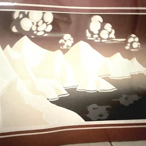 May include: A framed print of a stylized landscape with white mountains and a dark blue lake. The sky is a light brown with white clouds. The print is in a brown frame with a red mat.