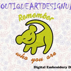 May include: Yellow embroidered design of a lion cub with the text "Remember who you are" in orange. The design is on a white background with a floral pattern.