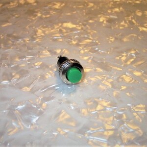 May include: A small, round, green push button switch with a silver metal housing.
