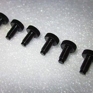 May include: Six black metal screws with hexagonal heads. The screws are arranged in a row on a white surface.