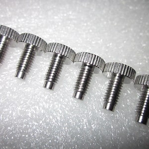 May include: Six silver-toned screws with a knurled head. The screws are arranged in a row from left to right, with the heads facing the viewer.