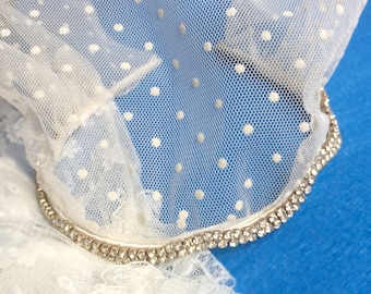 May include: White tulle fabric with polka dots and a silver rhinestone trim. The fabric is draped over a blue surface.
