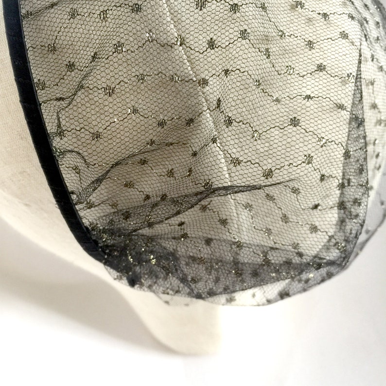 May include: Black tulle fabric with gold glitter accents. The tulle is gathered and has a black ribbon trim.