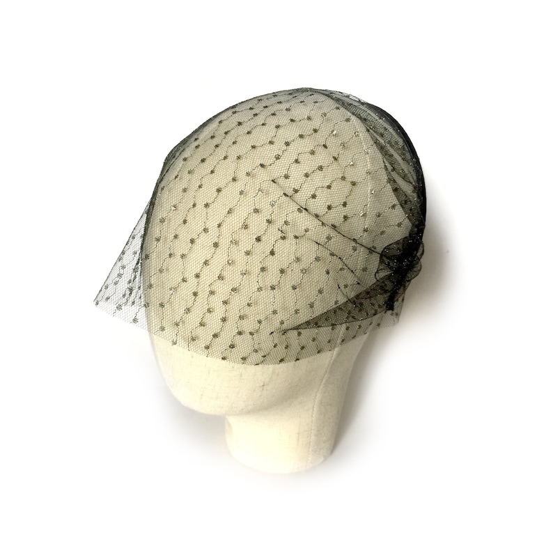 May include: A black tulle veil with gold glitter dots. The veil is on a white mannequin head.