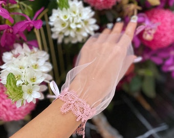 May include: A pink lace wristlet with a delicate floral design. The wristlet is made of sheer fabric and has a soft, feminine look.