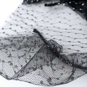 May include: Black tulle fabric with silver glitter dots. The fabric has a ruffled edge.