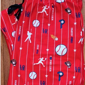 Może przedstawiać: Czerwono-białe, pasiasta piżama w stylu baseballowym. Spodnie mają r&oacute;żne grafiki związane z baseballem, w tym piłki, kije, rękawice i logo Philadelphia Phillies. Na spodniach nadrukowany jest tekst "FIGHTIN' PHILS" i "I LOVE PHILLIES".