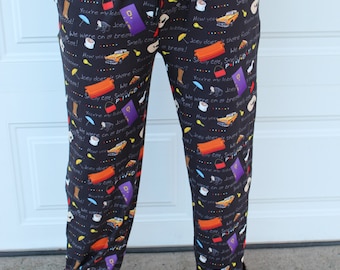 May include: Black pajama pants with a repeating pattern of text and images from the TV show "Friends". The text includes phrases like "Smelly Cat", "We were on a break", and "Joey doesn't share food".