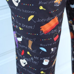 May include: Black pants with a repeating pattern of various images and text from the TV show Friends. The text includes phrases like "Smelly Cat", "We were on a break", "How you doin?", and "You're my lobster".
