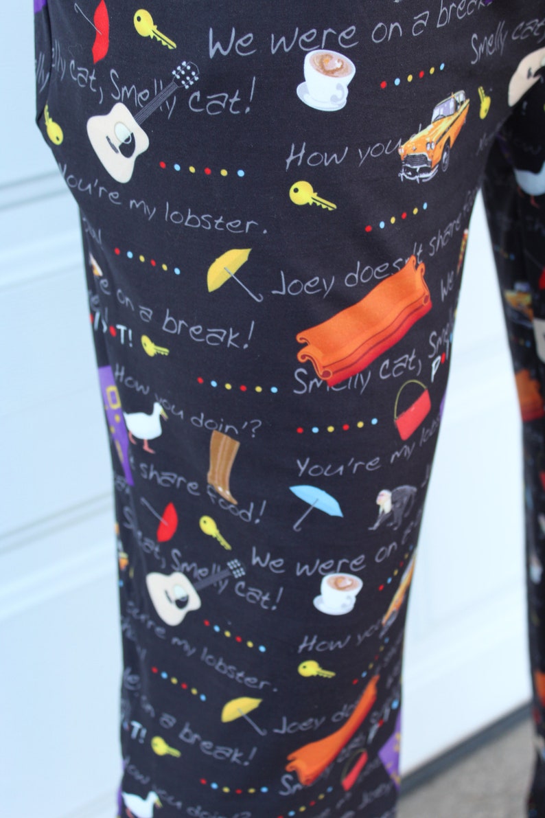 May include: Black pants with a repeating pattern of various images and text from the TV show Friends. The text includes phrases like "Smelly Cat", "We were on a break", "How you doin?", and "You're my lobster".