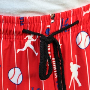 Może przedstawiać: Czerwono-białe, pasiasta piżama z motywem baseballowym. Spodnie mają czarny sznurek do ściągania i przedstawiają graczy w baseball, piłki baseballowe i napis "LOVE" nadrukowany na nich.