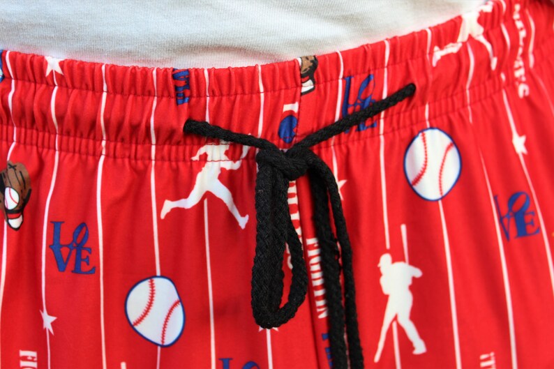 Może przedstawiać: Czerwono-białe, pasiasta piżama z motywem baseballowym. Spodnie mają czarny sznurek do ściągania i przedstawiają graczy w baseball, piłki baseballowe i napis "LOVE" nadrukowany na nich.