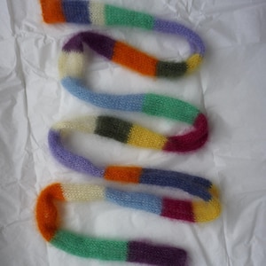 Può includere: Una sciarpa di lana soffice multicolore con strisce arancioni, viola, verdi, blu, gialle e bianche.