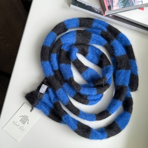 Könnte beinhalten: Blau-schwarzer gestrickter Schal mit einem weißen Etikett mit der Aufschrift "Wool On".