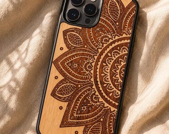 May include: A black smartphone case featuring a light-colored wood back panel with a dark brown laser-engraved mandala pattern. The design covers the majority of the rear surface, showcasing intricate floral and geometric details in a radial layout.