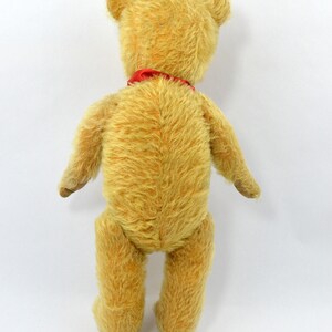 May include: A vintage teddy bear with a red ribbon around its neck. The bear is made of a soft, plush material and has a light brown color.