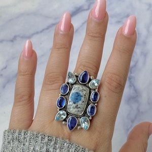 May include: A silver ring with a blue and white stone surrounded by smaller blue and white stones.