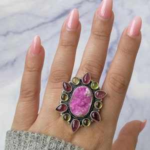 May include: A silver ring with a pink and green gemstone surrounded by smaller pink and green gemstones.