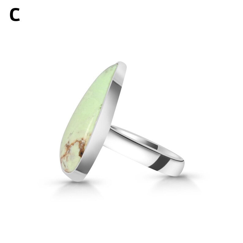 May include: A silver ring featuring a large, teardrop-shaped, pale green stone with brown matrix inclusions. The stone is set in a smooth, polished silver bezel, and the band is a simple, solid silver shank. The letter C is visible in the corner.