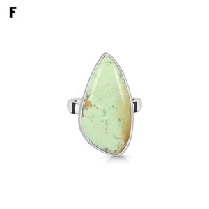 May include: A silver ring featuring a large, teardrop-shaped light green stone with natural dark veining and a small orange-brown inclusion at the base. The stone is set in a smooth, polished silver bezel that follows its irregular shape.