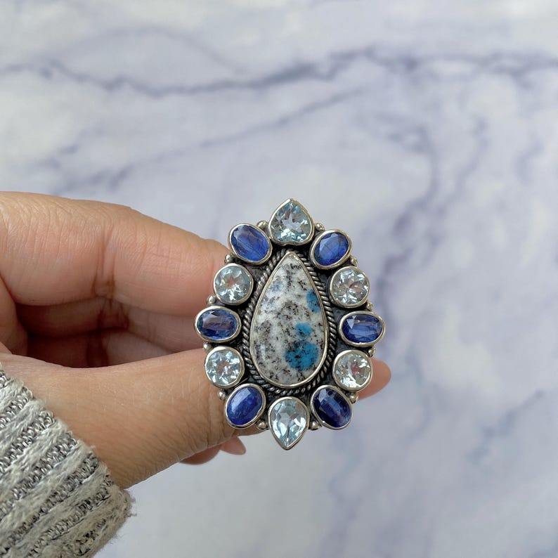 K&ouml;nnte beinhalten: Ein silberner Ring mit einem gro&szlig;en birnenf&ouml;rmigen blau-wei&szlig;en Edelstein, umgeben von kleineren blauen und wei&szlig;en Edelsteinen.