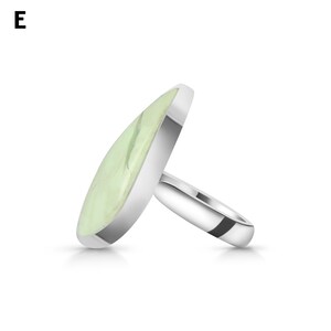 May include: A silver ring featuring a large, teardrop-shaped, pale green stone with subtle white veining set in a smooth metal bezel. The letter E is visible in the upper left corner. The ring band is polished silver and has a rounded profile.