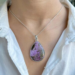 Puede incluir: Un collar de cadena de plata con un colgante en forma de lágrima con una piedra púrpura y marrón.