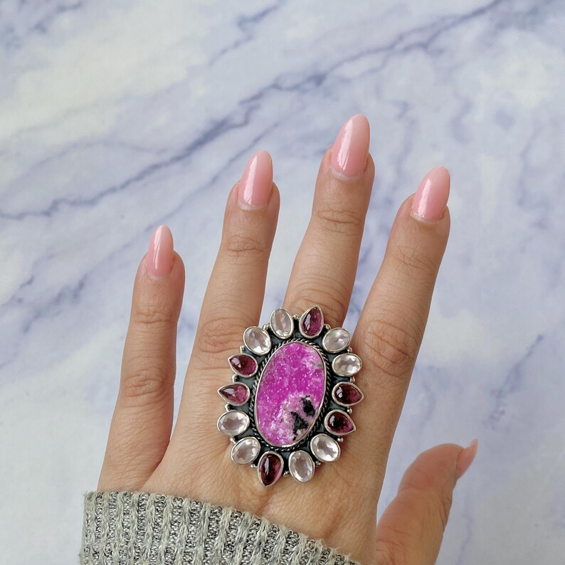 May include: A silver ring with a large pink and white oval gemstone surrounded by smaller pink and white gemstones.