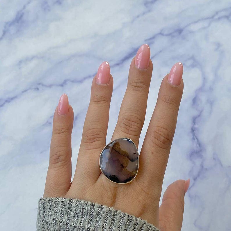 May include: A silver ring with a large, freeform, brown and gray agate stone. The ring is on a person's finger.