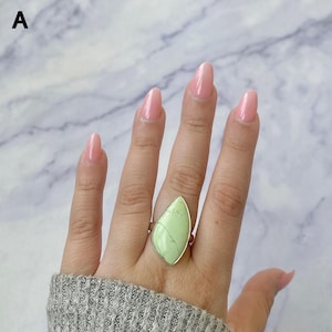 May include: A ring featuring a large, teardrop-shaped light green stone with visible dark veining, set in a simple silver-toned metal band. The stone has a smooth, polished surface and is positioned vertically on the finger for a bold look.