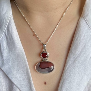 May include: A silver chain necklace with a pendant featuring a red gemstone and a larger oval-shaped agate stone with brown and white patterns.