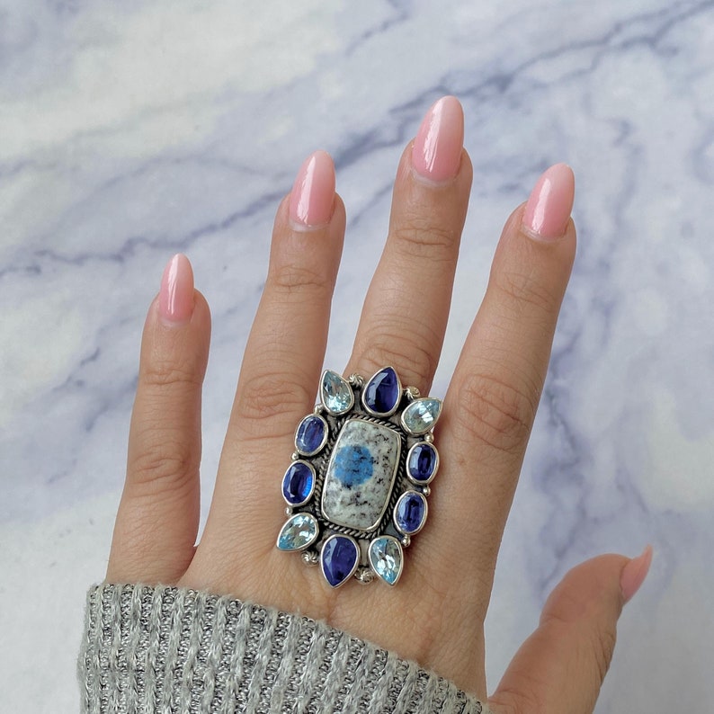May include: A silver ring with a blue and white stone surrounded by smaller blue and white stones.