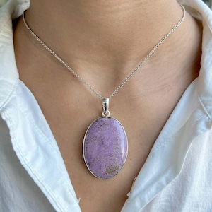 Puede incluir: Un collar de cadena de plata con un colgante ovalado morado. El colgante está hecho de una piedra natural con un patrón único.