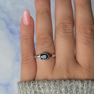 May include: A silver ring with a black oval-shaped stone. The ring is set in a simple, classic style, with a polished band. The stone is the focal point, creating a minimalist and elegant design.
