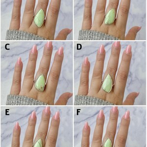 May include: A collection of six silver rings, labelled A through F, each featuring a unique, teardrop-shaped light green gemstone set in a smooth metal bezel. The stones display natural variations in colour, veining, and texture across the set.