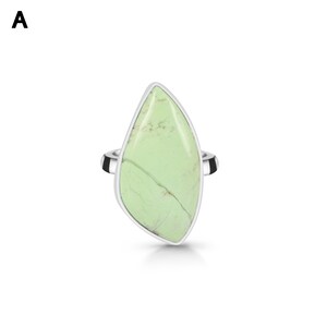 May include: A silver ring featuring a large, asymmetrical, light green stone with visible dark veining. The stone is set in a smooth, polished silver bezel that follows the irregular, elongated shape of the gemstone, mounted on a simple silver band.