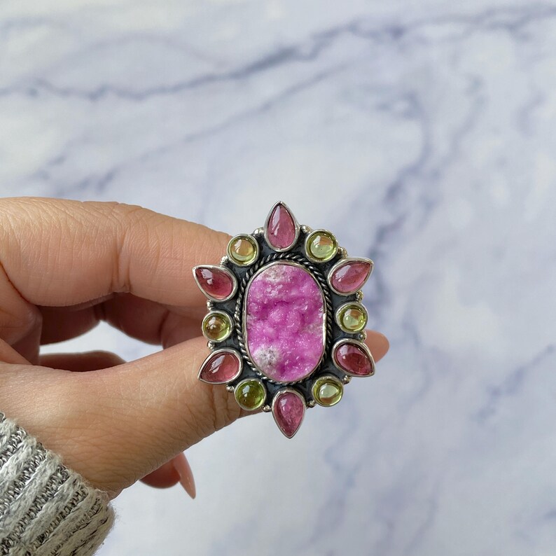 May include: A silver ring with a large pink and white gemstone surrounded by smaller green and pink gemstones.