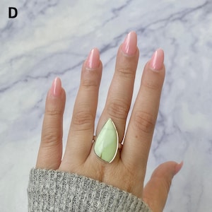 May include: A silver ring featuring a large, teardrop-shaped, light green stone set in a smooth metal bezel. The stone displays subtle natural veining and a matte finish. The letter D is visible in the upper left corner of the image.