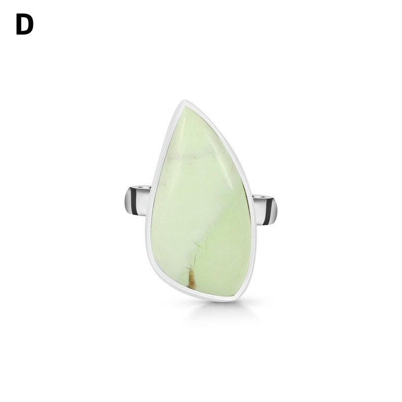 May include: A silver ring featuring a large, asymmetrical, teardrop-shaped pale green stone with subtle white veining. The metal band is visible on both sides of the stone, which is set in a smooth, polished silver bezel frame. The letter D is visible.