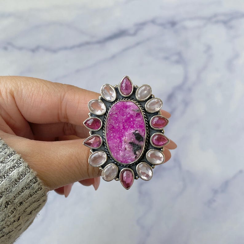 May include: A silver ring with a large pink and white oval gemstone surrounded by smaller pink and white gemstones.